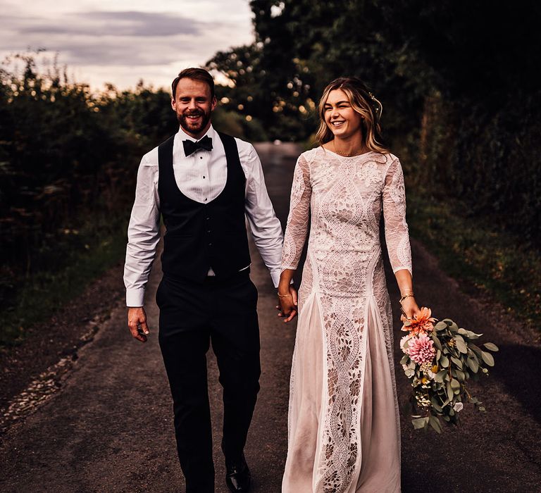 Groom walks along with the bride in a boho wedding dress for their marquee wedding 