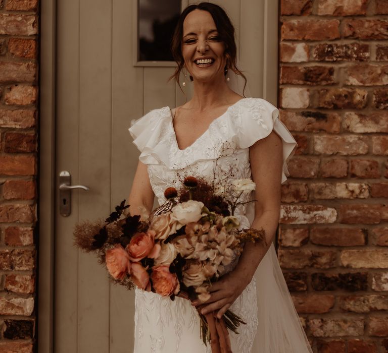 Ruffle embroidered floral wedding dress holding a pink and muted tones wedding bouquet with pearl drop earrings