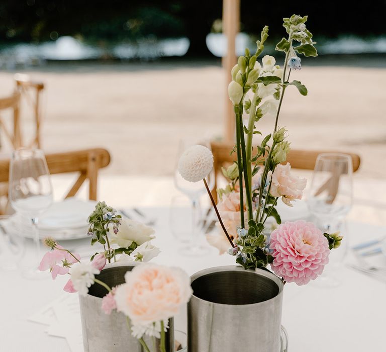 Pastel floral centrepieces in metal vases on rounded tables surrounded by wooden chairs