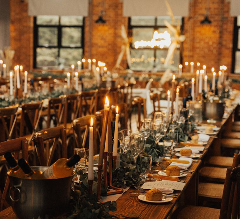 Green foliage table runners line wooden banquet tables at the Venue Bowers Mill