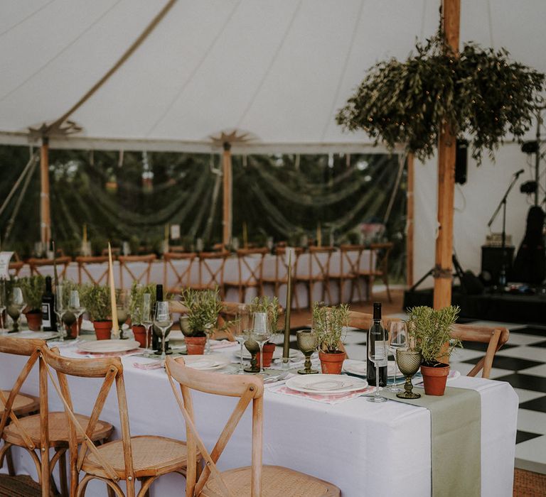 Terracotta plant pots of rosemary decorating the banquet tables with green table runner and wooden chairs in a white marquee 