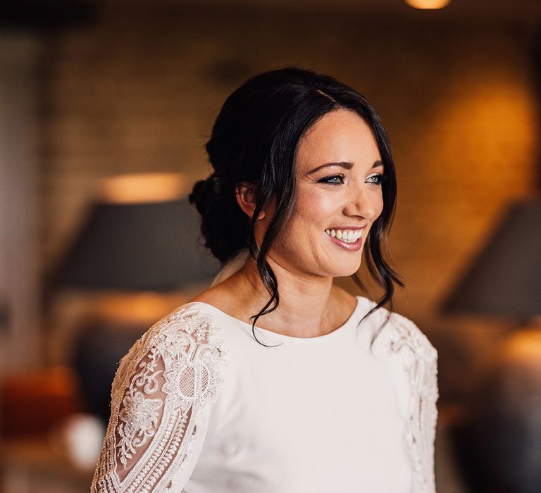 Smiling bride with dark hair in an updo wearing a lace and beaded long sleeve Atelier Pronovias wedding dress 