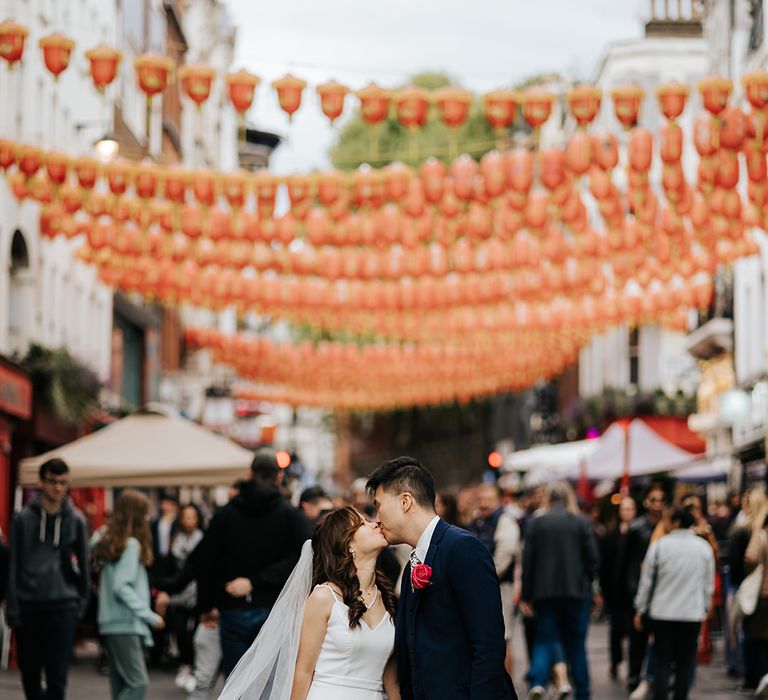 Bride wearing fitted white classic wedding dress kisses her groom in China Town London on their wedding day