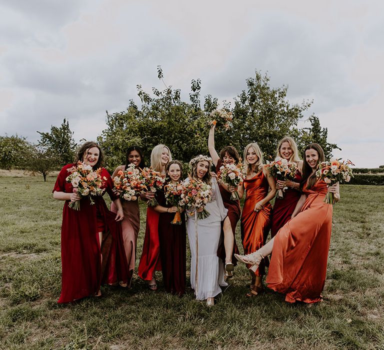 Bride stands with bridesmaids in Autumn colour bridesmaid dresses with boho feel in outdoor wedding photos