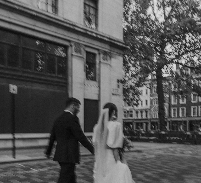 Bride in v neck wedding dress with front slit and groom in dark suit walking around Somerset House