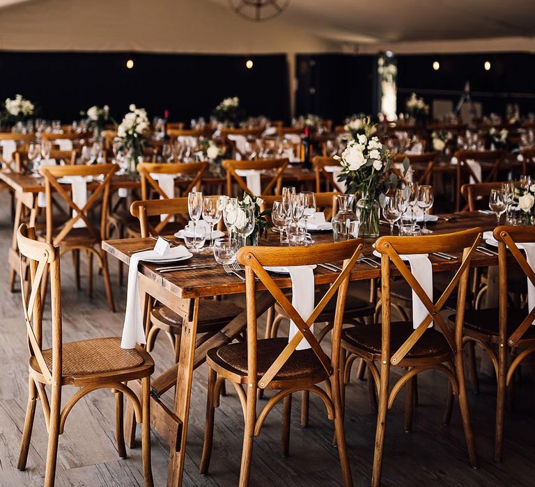 Minimal wooden banquet tables and chairs with white tableware under a marquee