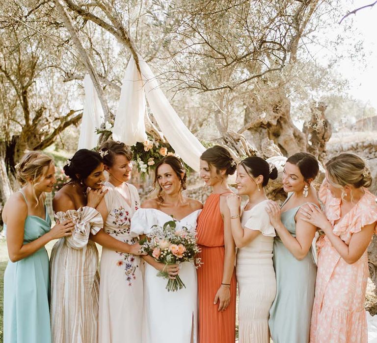 The bride poses with her bridal party for destination wedding with mismatched bridesmaid dresses 