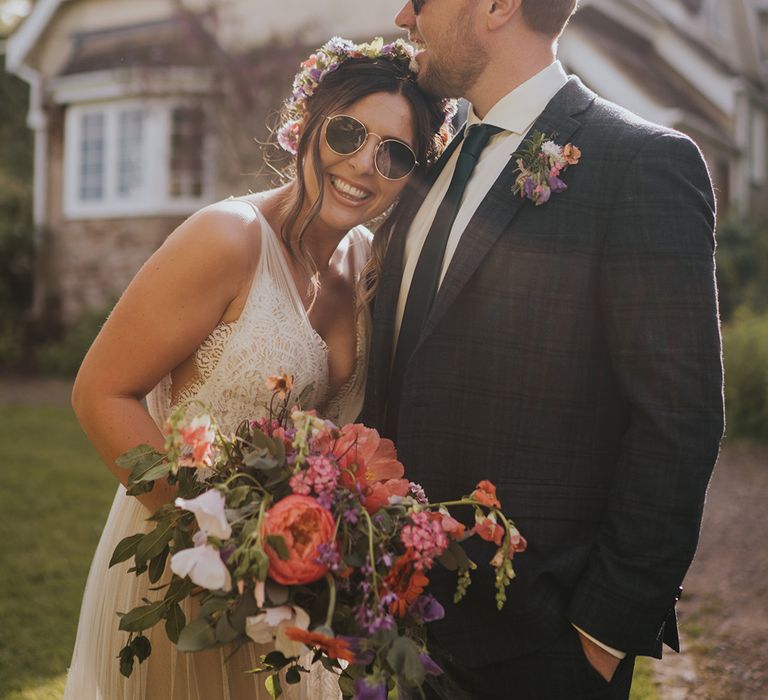 Bride wears colourful flower crown and sunglasses on her wedding day outdoors 