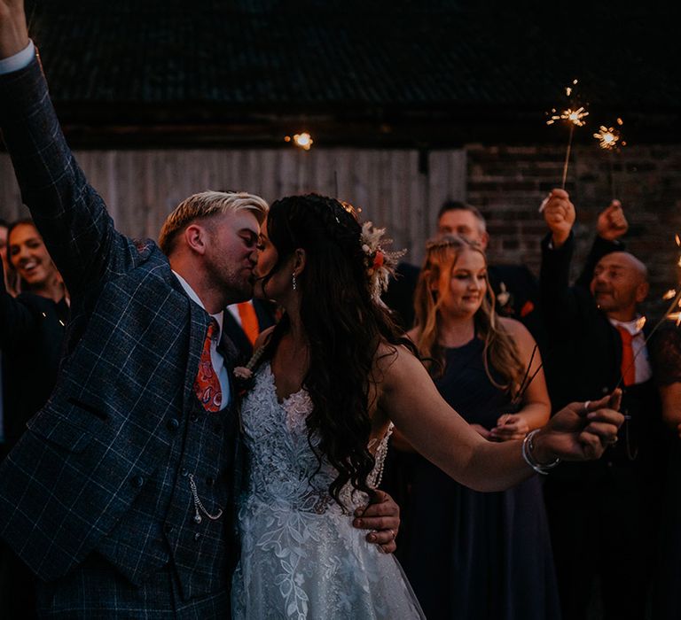 The bride and groom share a kiss as they wave their sparklers together at the end of their wedding day 