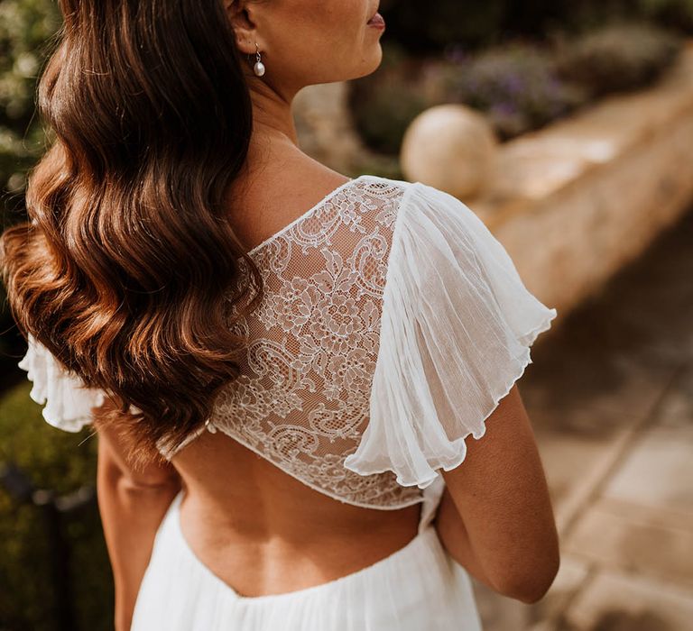 Bride showing open-back lace detailing of silk vegan wedding dress and pearl drop earrings