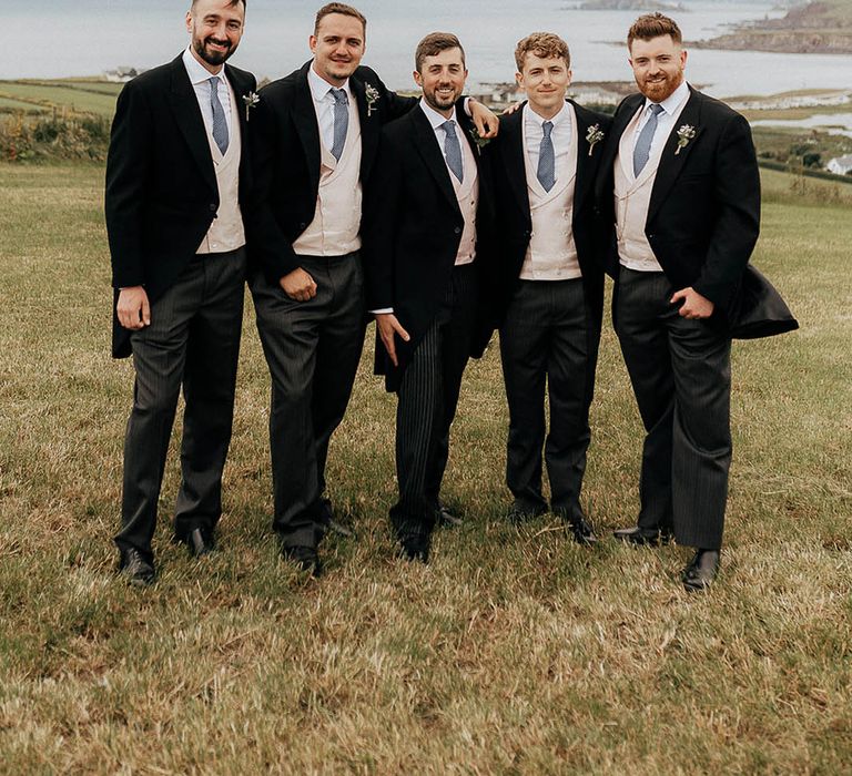 Groom and his groomsmen wear pale pink waistcoats and blue ties with floral buttonholes 