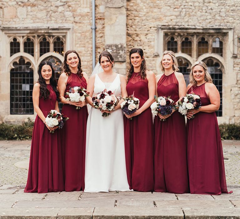 Bridesmaids in illusion neckline burgundy dresses holding matching bouquets with the bride in a Maggie Sottero wedding dress 