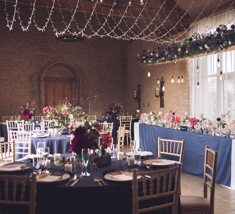 Stratton Court Barn Bicester wedding venue with fairy lights with blue, purple, pink and red wedding flowers and hanging festoon lighting 