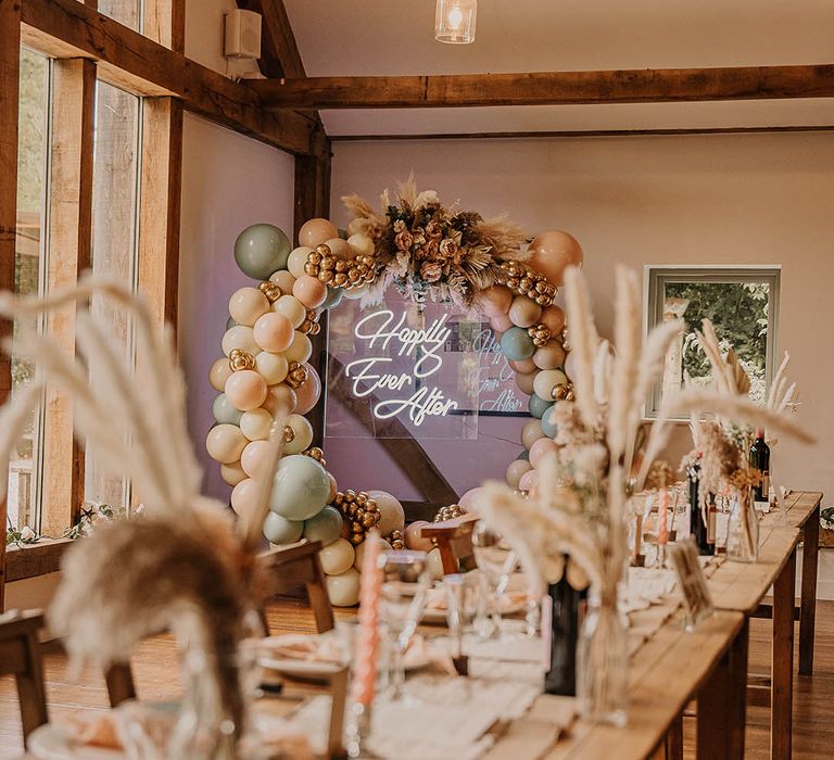 Green, pink, white, and gold wedding balloon arch decoration with a white neon sign decorating the rustic barn wedding venue 