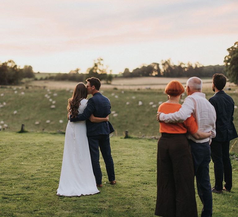 Groom in navy suit kisses the bride on the forehead as they look out at the views in the Lake District 