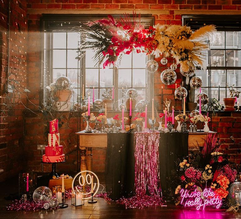 Colourful wedding tablescape with pink metallic streamers, hanging disco ball decorations, hot pink neon wedding sign, yellow smiley face neon sign, viva magenta, fuchsia and hot pink tapered candles and suspended pink and yellow rose flowers with foliage 