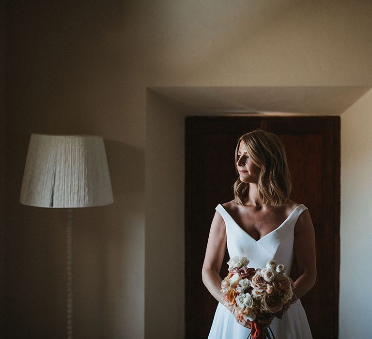 Bride in Suzanne Neville wedding dress holds pastel rose bouquet tied with red ribbon