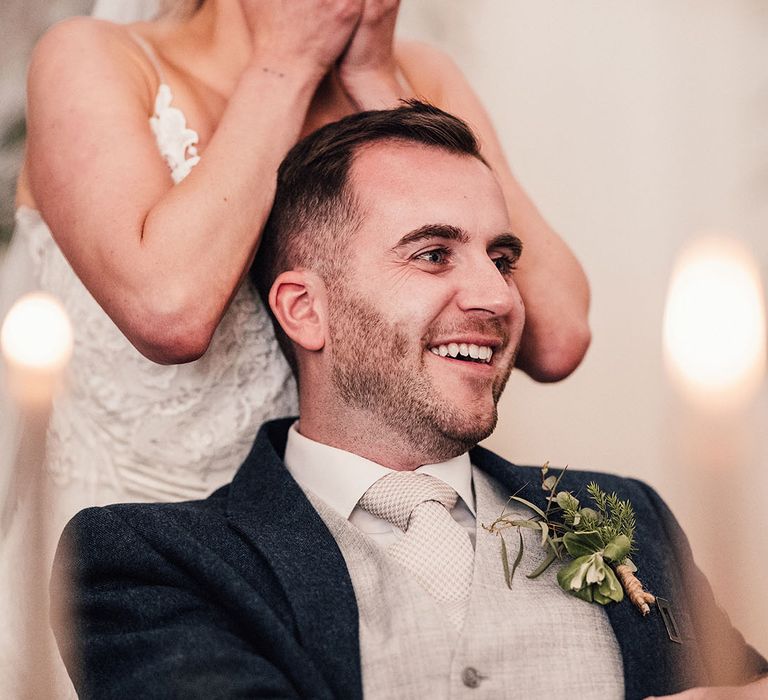 The bride with metallic silver wedding nails looks shocked as the groom in a navy suit chuckles listening to wedding speeches 