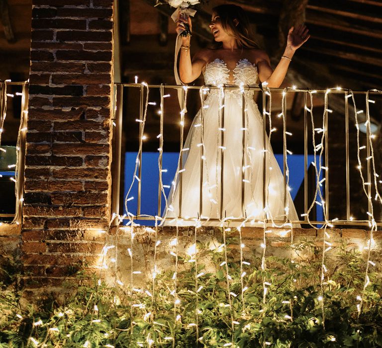 Bride preparing for bouquet toss on balcony with fairy lights wedding lighting