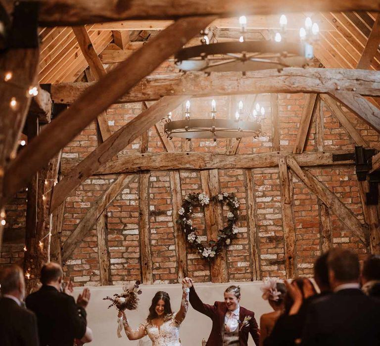 Brides raising their arms and walking out of Bassmead Manor Barns wedding venue to music 