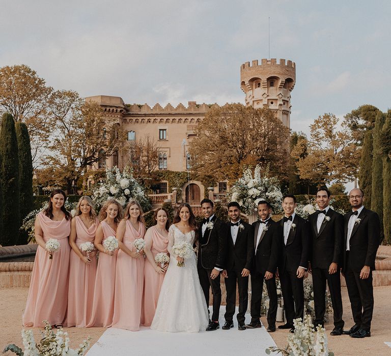 Bridesmaids in dusky pink bridesmaid dresses and groomsmen in classic black suits with bride and groom at castle wedding venue 