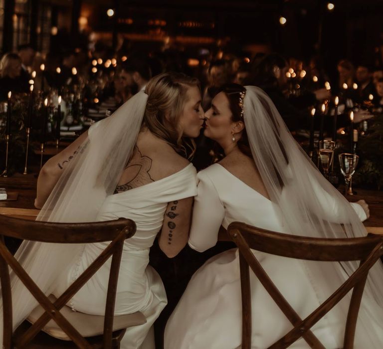 Bride in satin short sleeve deep v wedding dress and church length veil and bride in long sleeve deep v wedding dress and church length veil kissing at rustic wedding tablescape at Hidden River Cabins 