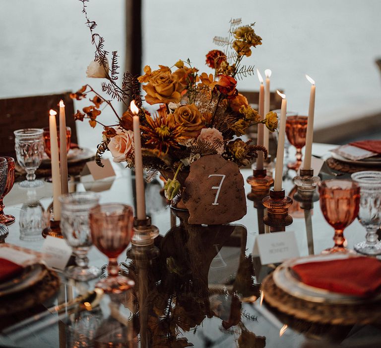 Luxury beach wedding with an autumnal rustic style table number sign surrounded by warm toned florals and taper candles 