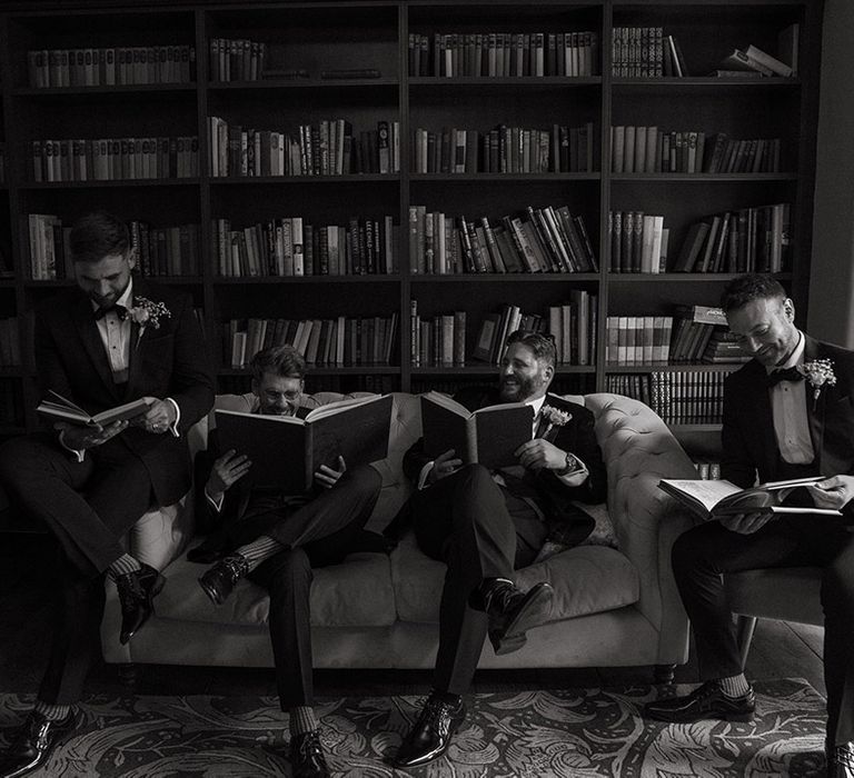 Groomsmen pose together in the morning as they get ready for the wedding reading books 