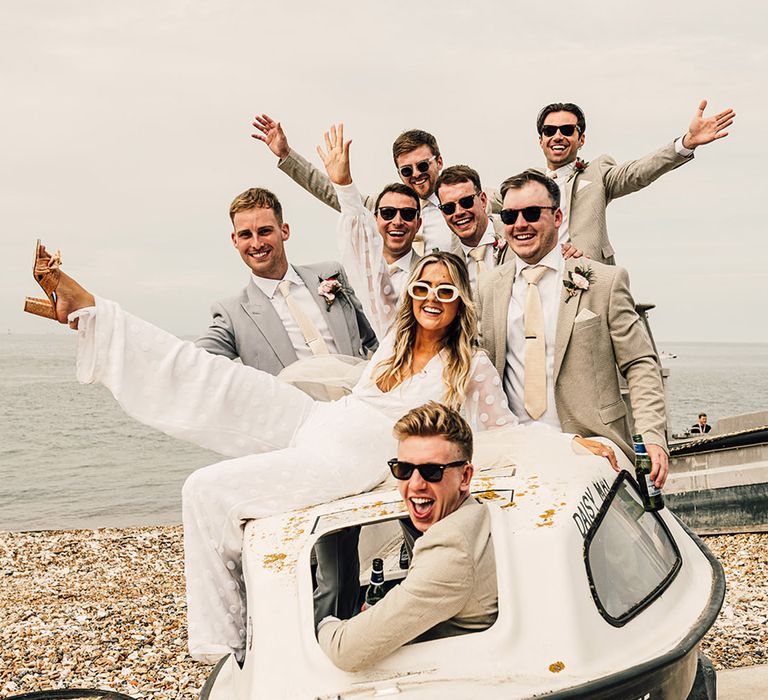 coastal wedding at East Quay Whitstable with bride, groom and groomsmen sitting in a boat on the beach 