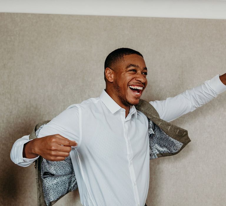 Groomsmen puts on his light grey double breasted suit jacket 