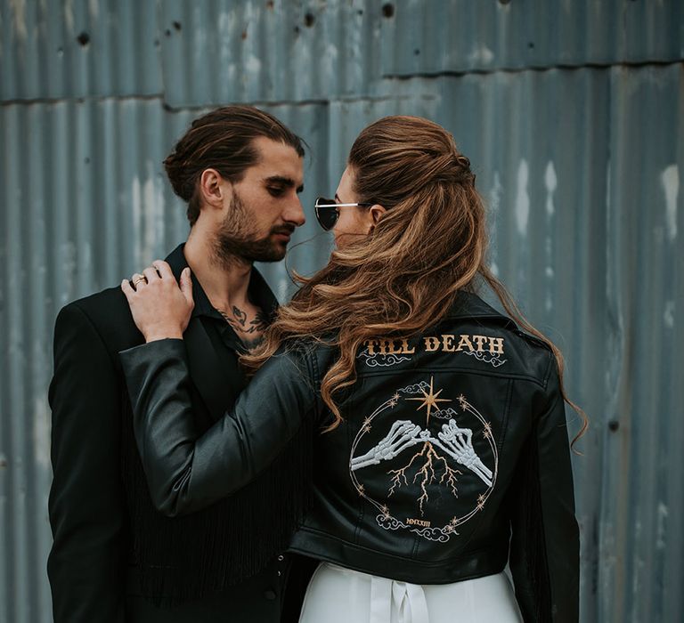 Bride wearing black bridal leather jacket with bespoke design on the back gazing into the groom's eyes 