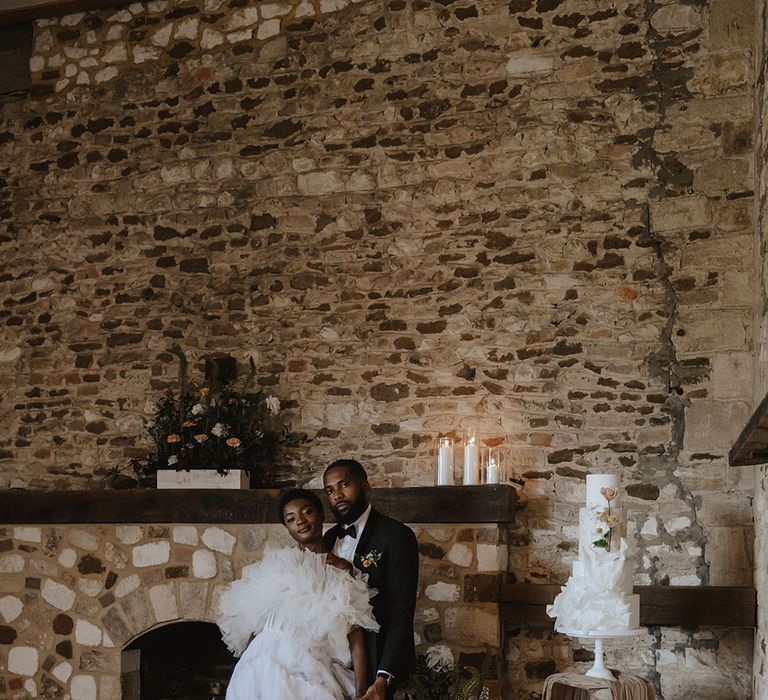 Bride and groom pose next to white three tier wedding cake with ruffle detail to match the wedding dress 