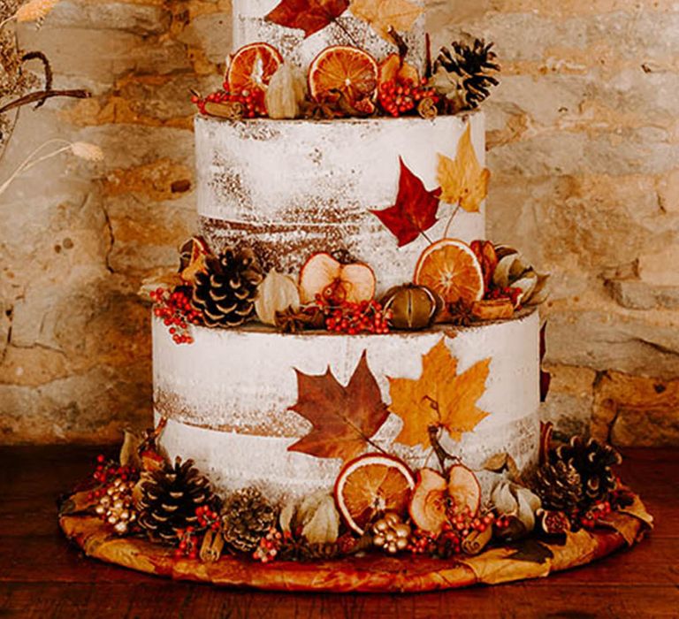 Three tier rustic wedding cake decorated with white icing and autumn leaves, berries and pinecones 