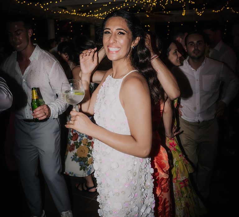 Bride in short wedding reception dress with large white sequins smling whilst holding a gin and tonic