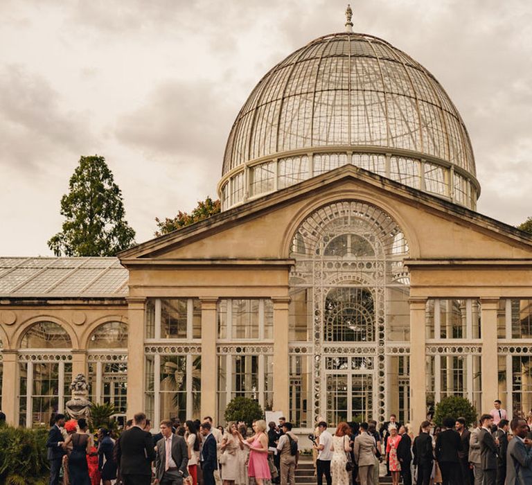 Wedding guests have drinks mingling on front lawn at country house wedding venue 