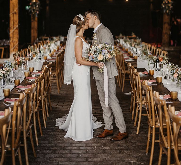 Rustic wedding venue with the bride and groom sharing a kiss surrounded by pastel wedding decor 