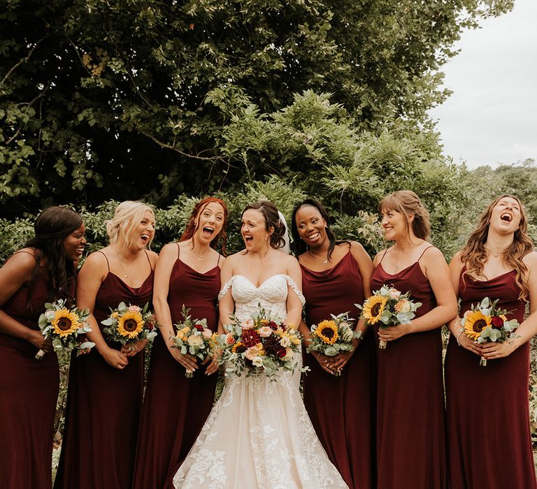 Bridesmaids wearing burgundy red bridesmaid dresses with sunflower bouquets with the bride in a mermaid wedding dress