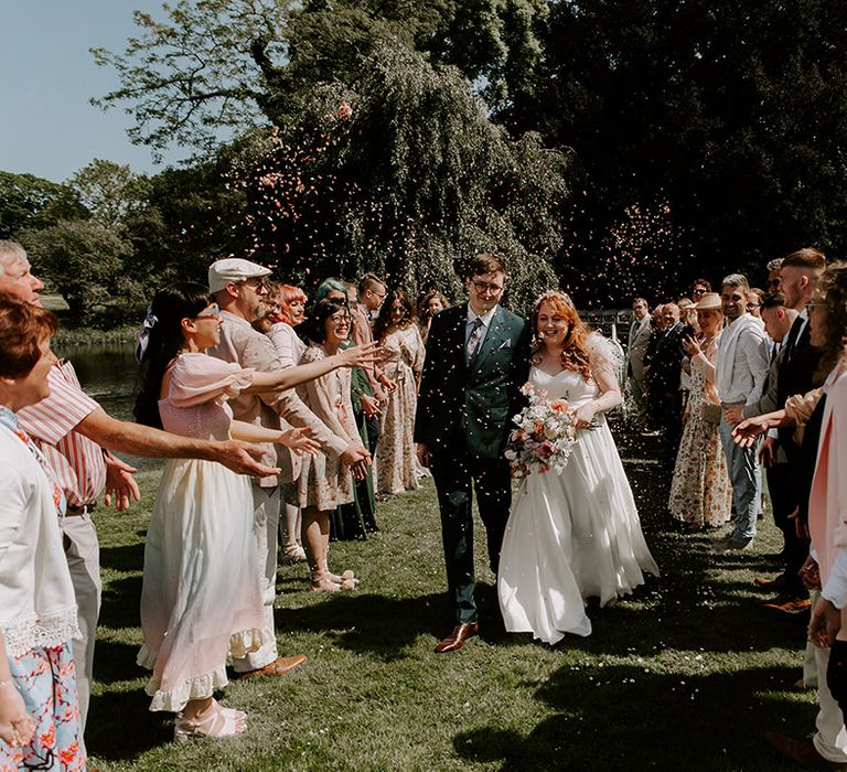 Two rows of guests throw confetti over the bride and groom in celebration 