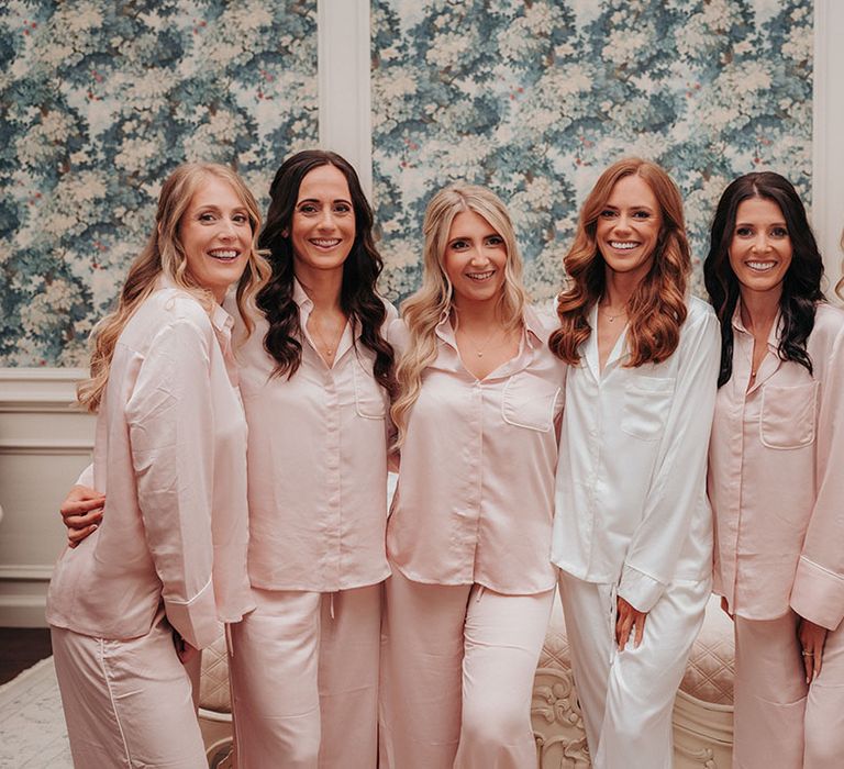 Bridesmaids in light pink pyjamas with the bride in white pyjamas as they get ready for the wedding 