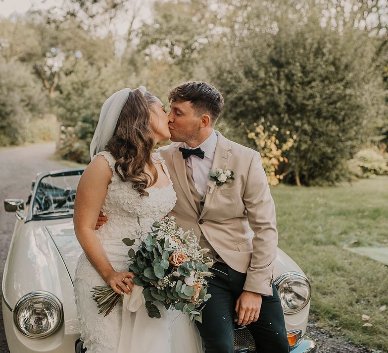 Groom in beige suit jacket with white rose buttonhole and black bow tie with the bride in a custom wedding gown with a rose wedding bouquet 