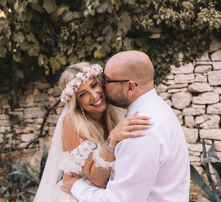 Groom kisses bride on the cheek who is wearing flower crown hair accessory 