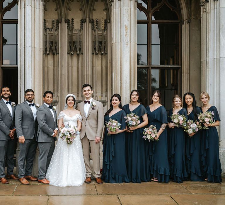 Group wedding party photo with bridesmaids in navy dresses and groomsmen in grey suits with black bow ties 