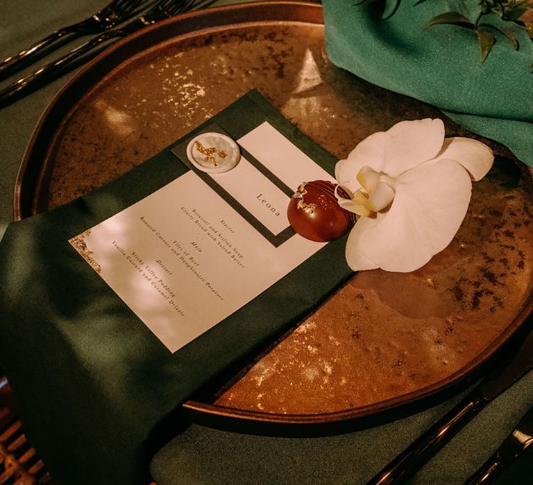 Circular gold charger plate with dark green wedding menu and place name for green wedding theme idea 