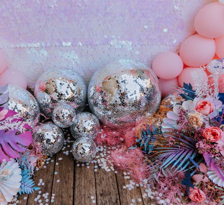 Holographic pastel wedding decor with sequin backdrop, disco balls and coloured monstera leaves