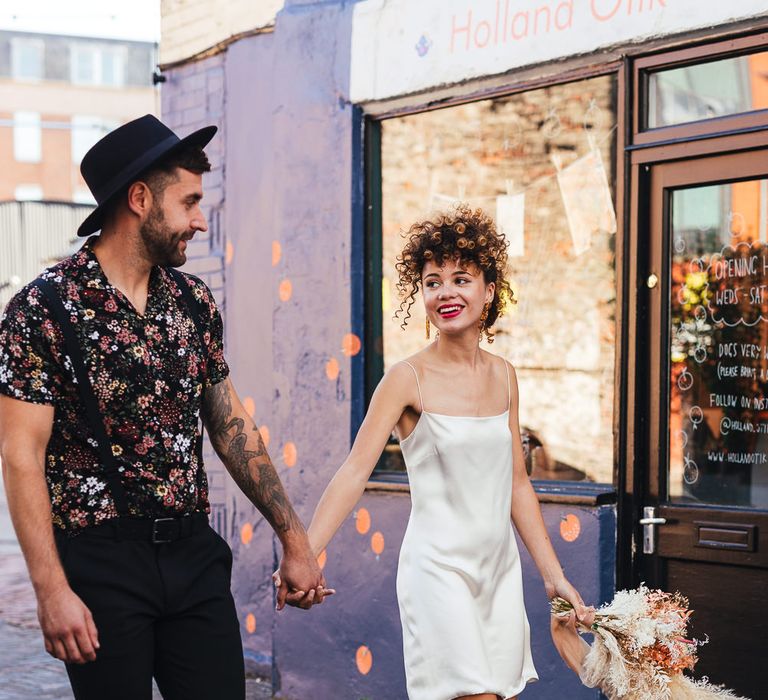 Stylish bride and groom holding hands walking down the street 