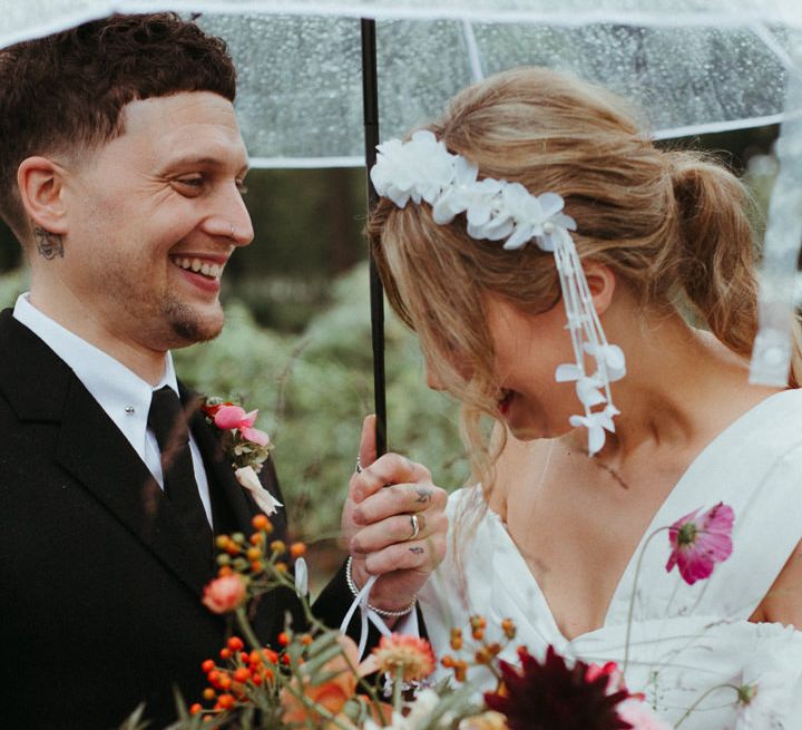 Colourful wedding bouquet with bride wearing ruffled headband as groom smiles