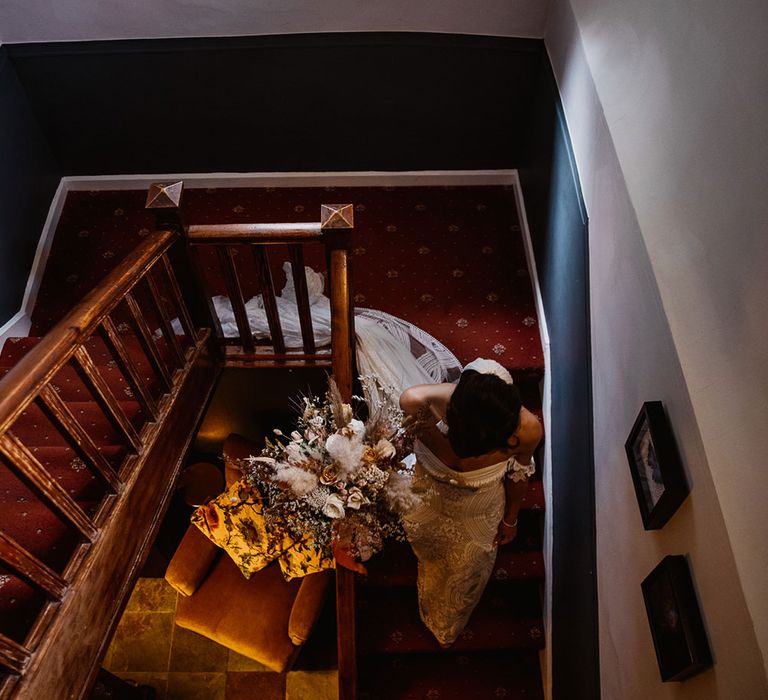 Bride in Rue de Seine dress walks down stairs holding white rose and pampas grass bouquet