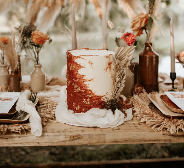 Wedding cake with burnt orange and white frosting complete with gold leaf decor 