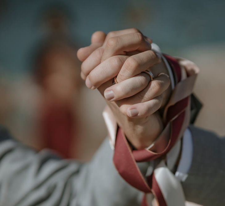 The grooms hold hands tightly while tied with a red ribbon