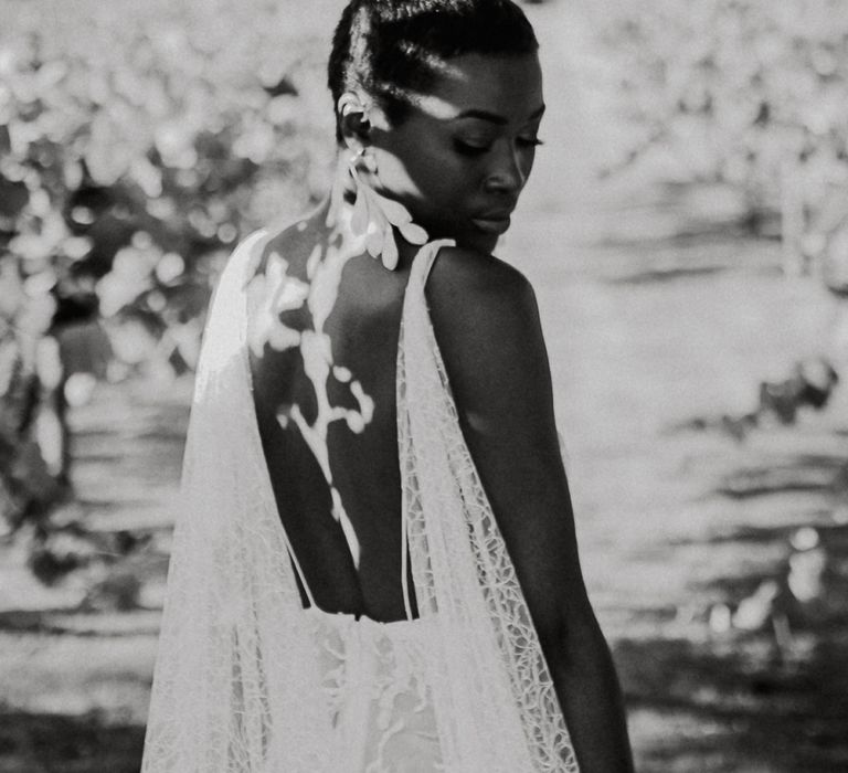 Black and white portrait of a bride standing in the sun with short hair, dangling earrings and watteau train wedding dress